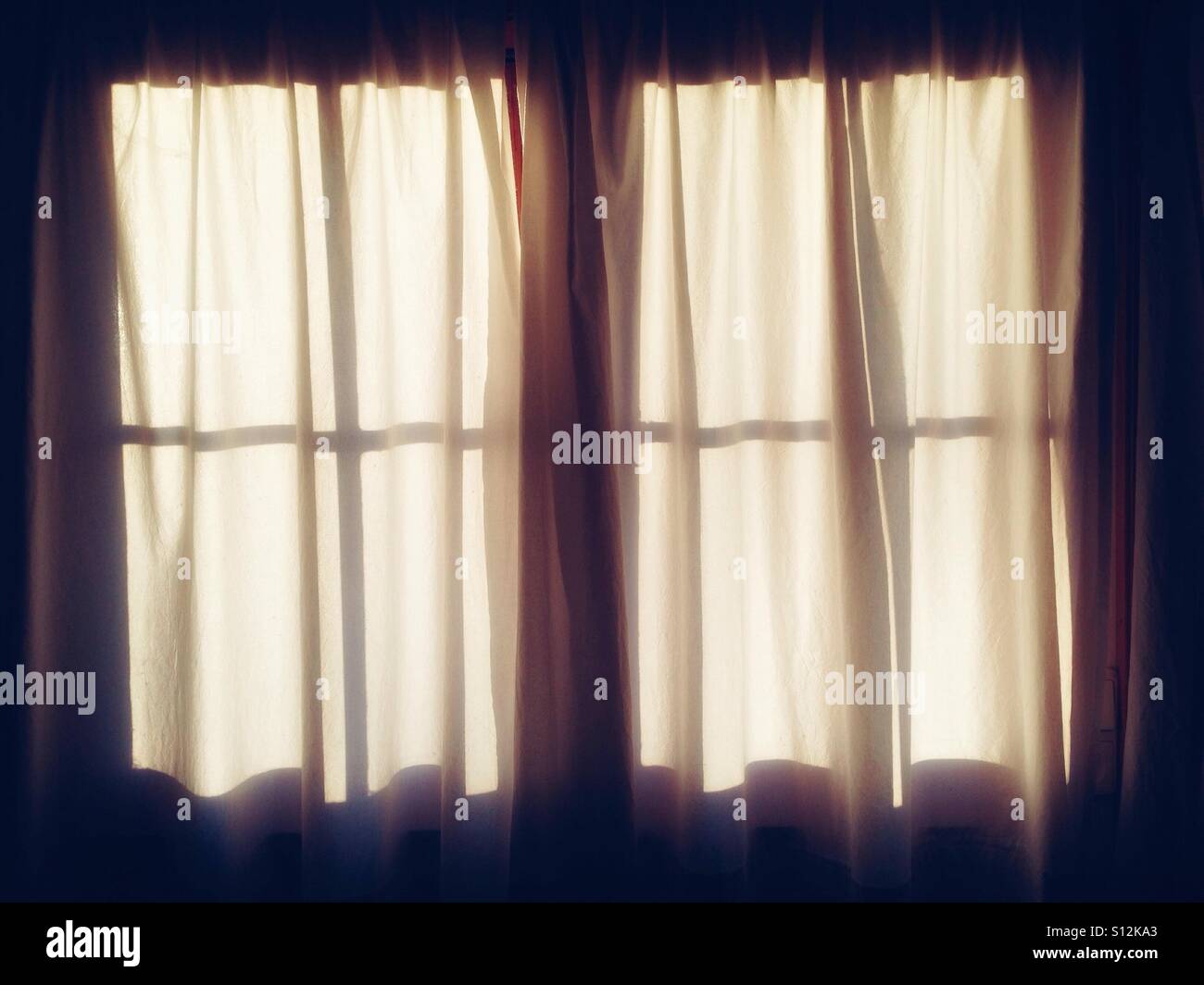 Ein Oberlicht-Fenster mit weißen Vorhängen im sanften Licht der Morgensonne Stockfoto