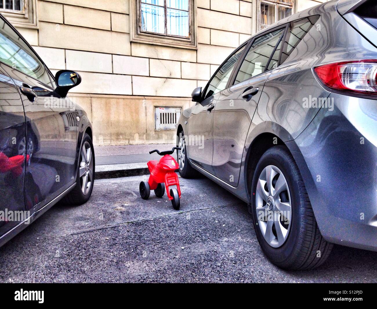 Kinder balancieren Zyklus zwischen zwei Autos auf einem Parkplatz geparkt - Smartphone-aufgenommenes Stockfoto
