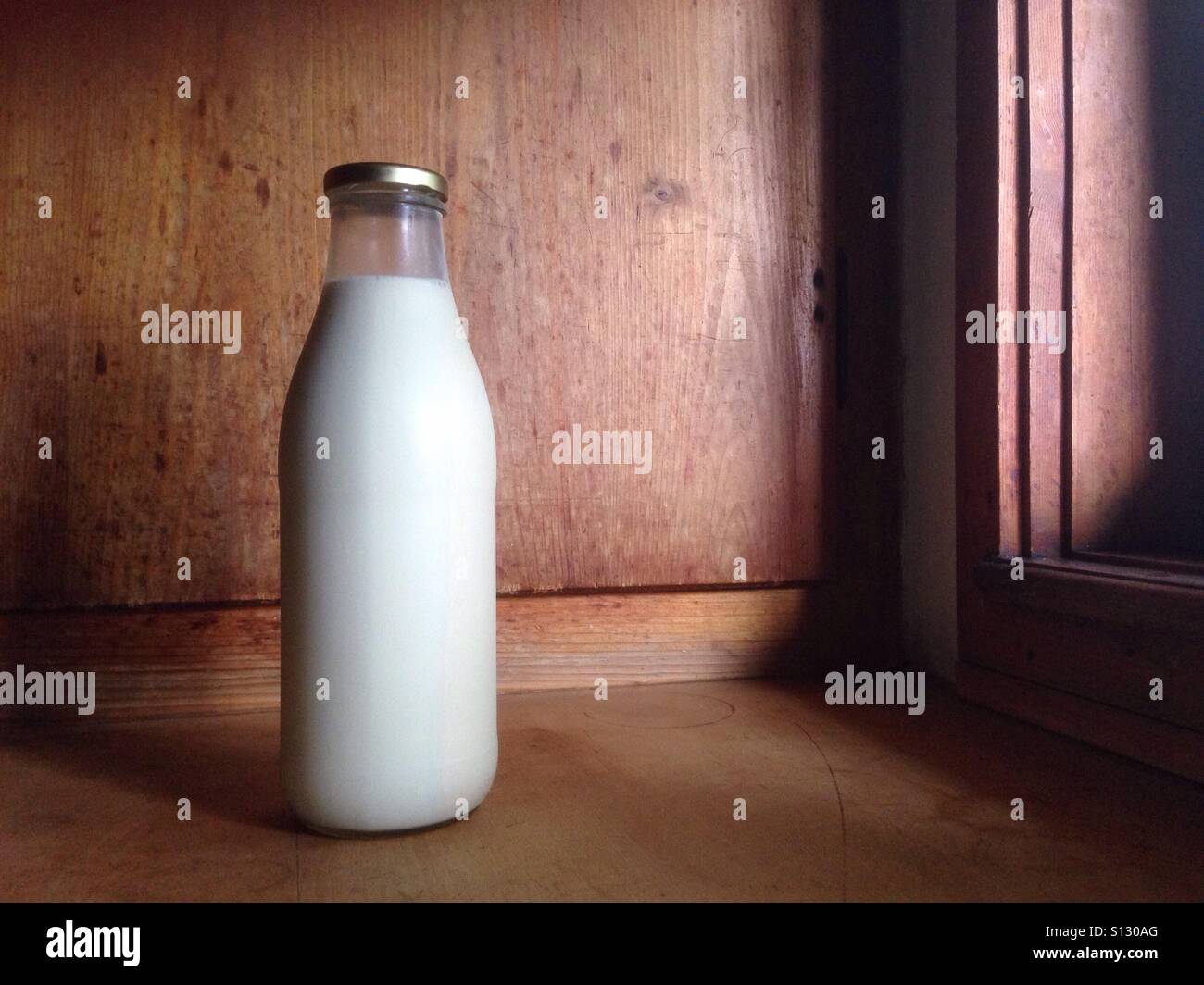 Eine altmodische Milch Flasche stehend auf einer Holzfläche mit sanfter Beleuchtung aus einem Fenster Stockfoto
