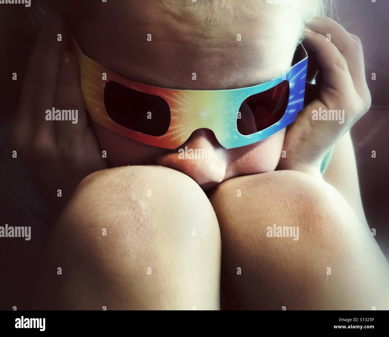 Ein Kind mit 3D Brille hat seine Nase zwischen die Knie gequetscht. Stockfoto