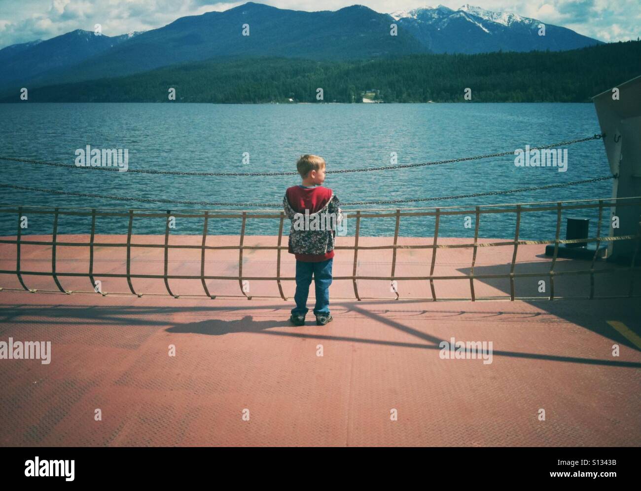 Ein kleiner Junge steht allein an der Front eine Überfahrt mit einen Bergsee. Stockfoto