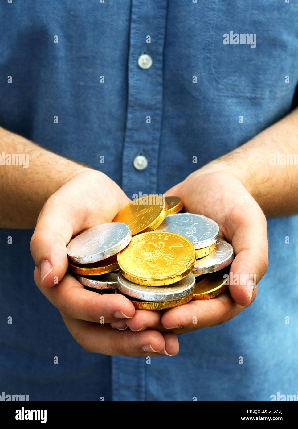 Ein paar Hände halten eine Handvoll gold und Silber Schokoladen-Münzen. - Smartphone-aufgenommenes Stockfoto