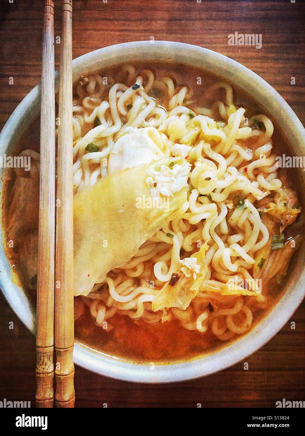 Nudeln mit Suppe und Kimchi in einer Schüssel mit Stäbchen auf der Seite ausgeglichen. - Smartphone-aufgenommenes Stockfoto