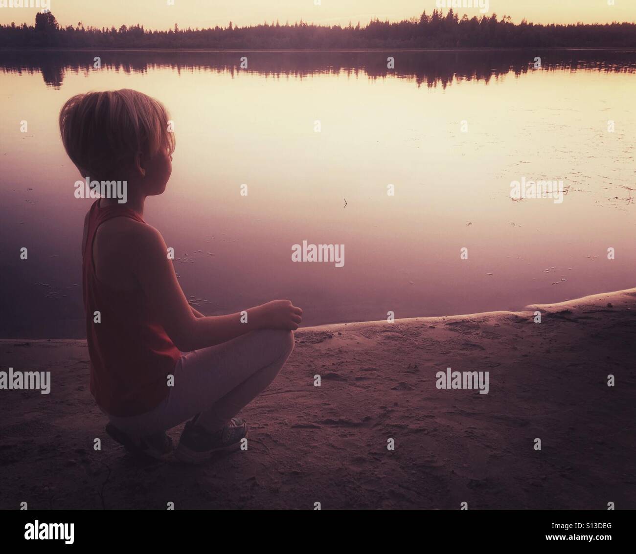 Ein junges Mädchen beobachtet den Sonnenuntergang vom Ufer eines kleinen Sees. Stockfoto