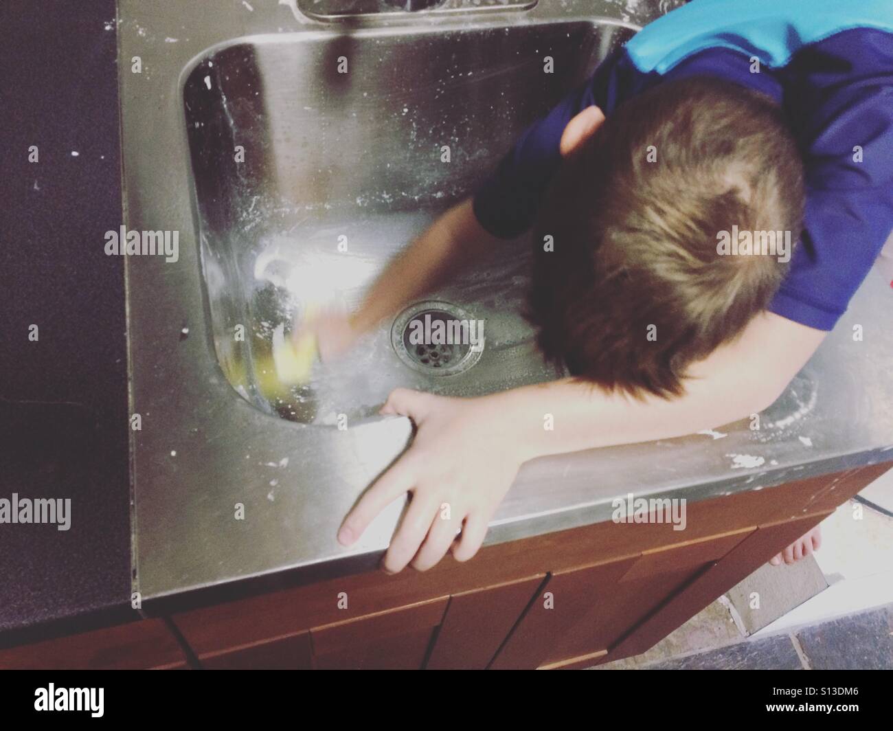 Junge tun Hausarbeiten und ein Waschbecken schrubben Stockfoto