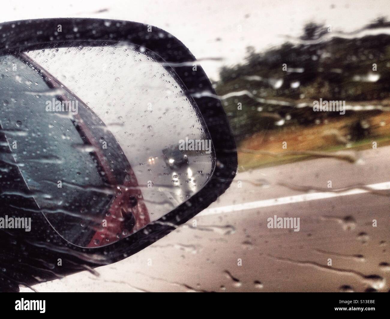 Außenspiegel an einem regnerischen Tag auf einer deutschen Autobahn mit einem herannahenden Auto Stockfoto