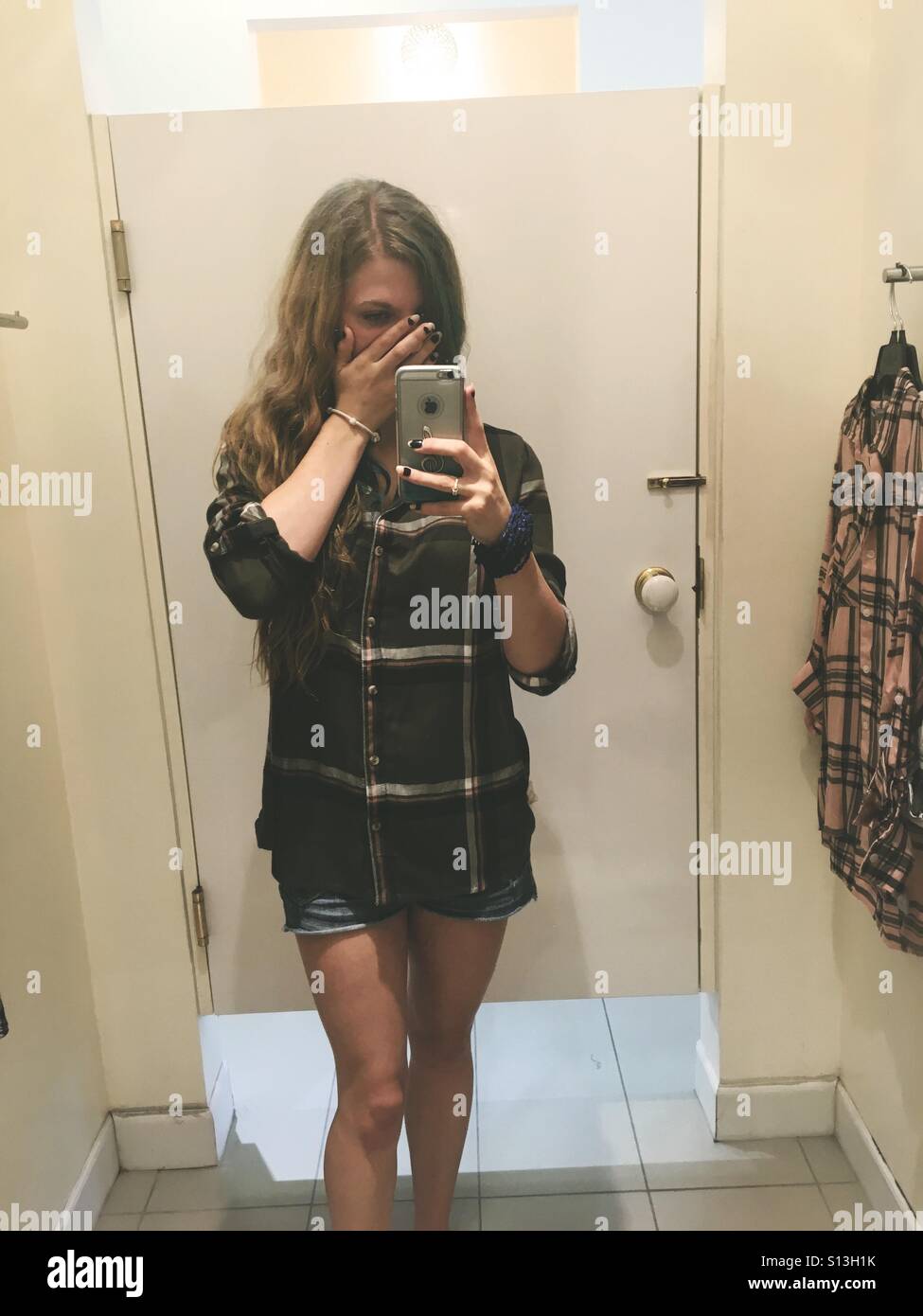 Teengirl in Flanell Hemd und Jean Shorts bedeckte ihr Gesicht und posieren,  eine Spiegel Selfie in der Mall, die Umkleidekabine zu nehmen  Stockfotografie - Alamy