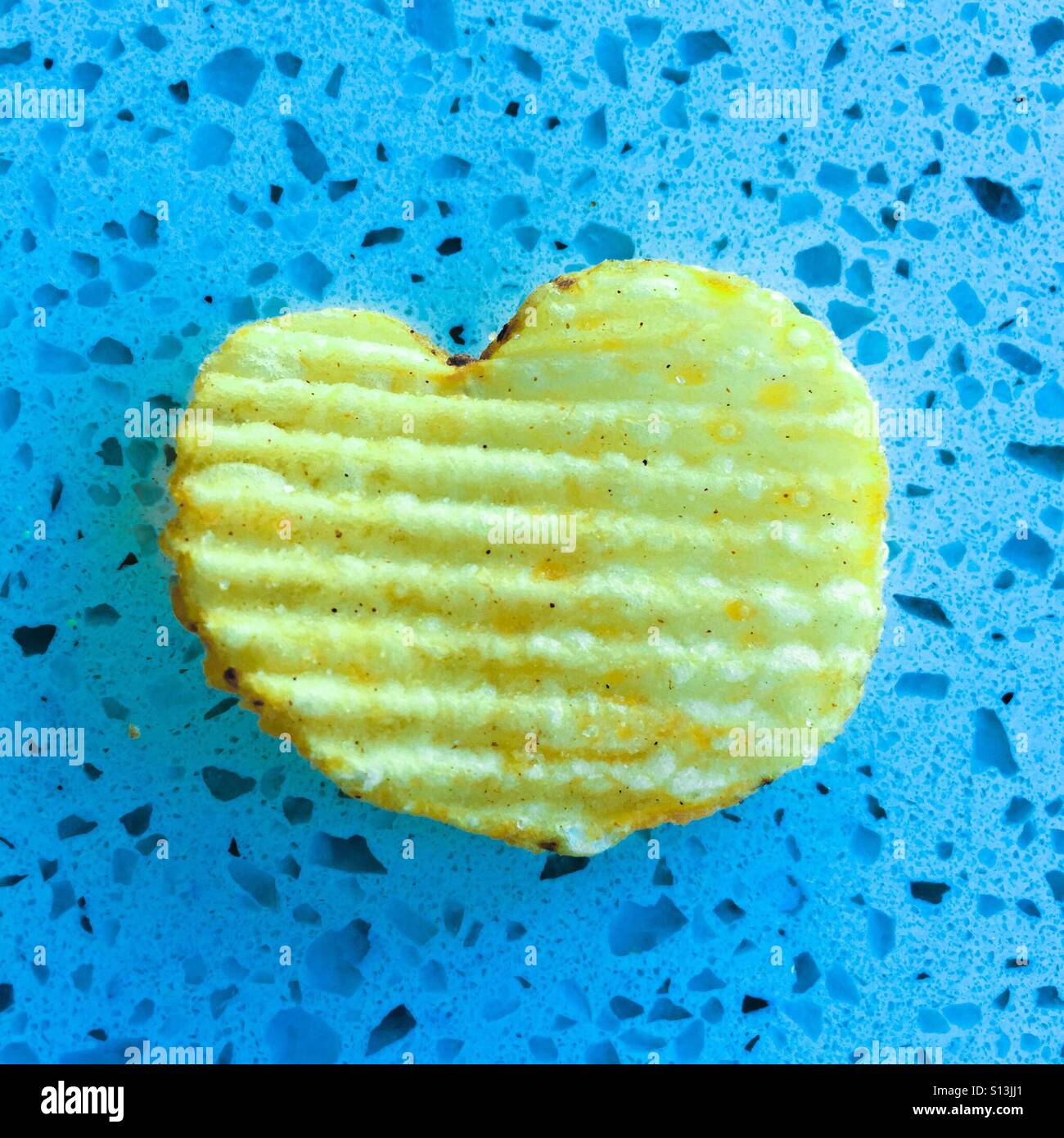 Eine herzförmige Kartoffel-Chips knusprig auf blauem Grund. Stockfoto