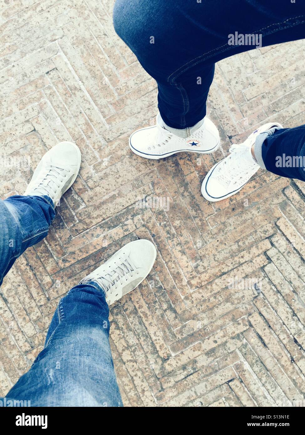 Blick von oben auf Mann und Frau, die Seite an Seite in Jeans und weißen Sneakers gehen - Smartphone-aufgenommenes Stockfoto