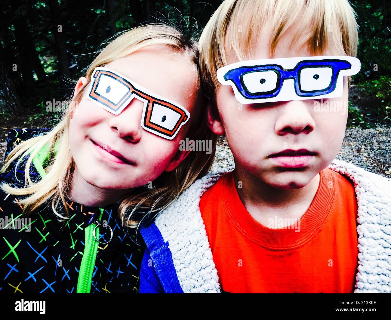 Zwei Kinder bedecken ihre Augen mit Aufklebern, die aussehen wie Gläser als Teil ihres Spiels. Stockfoto