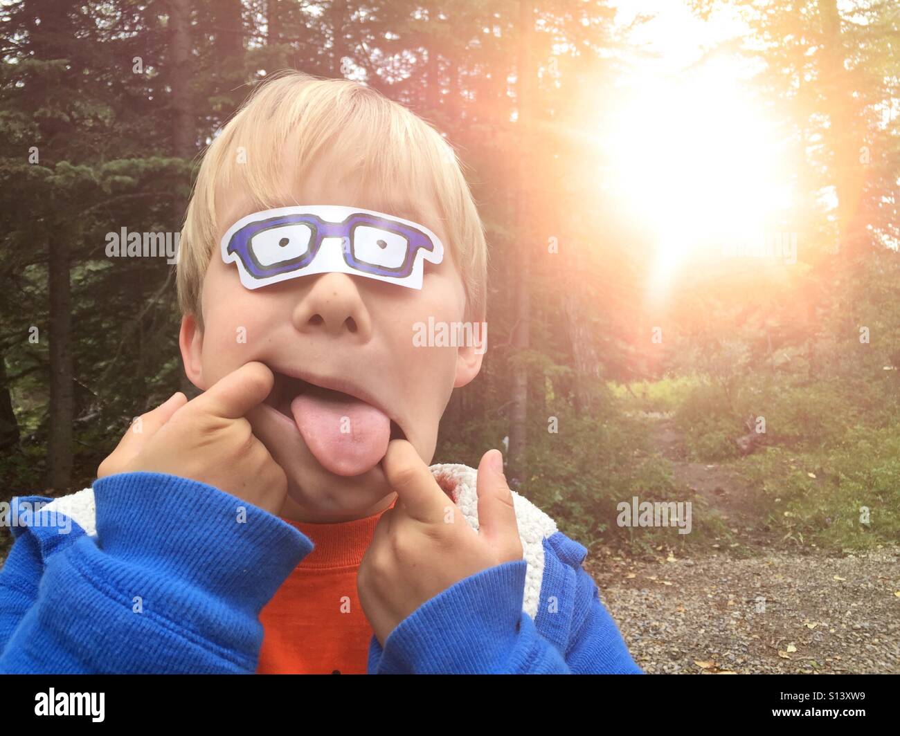 Ein Junge steckt seine Zunge machen ein lustiges Gesicht, spielen im Freien. Stockfoto