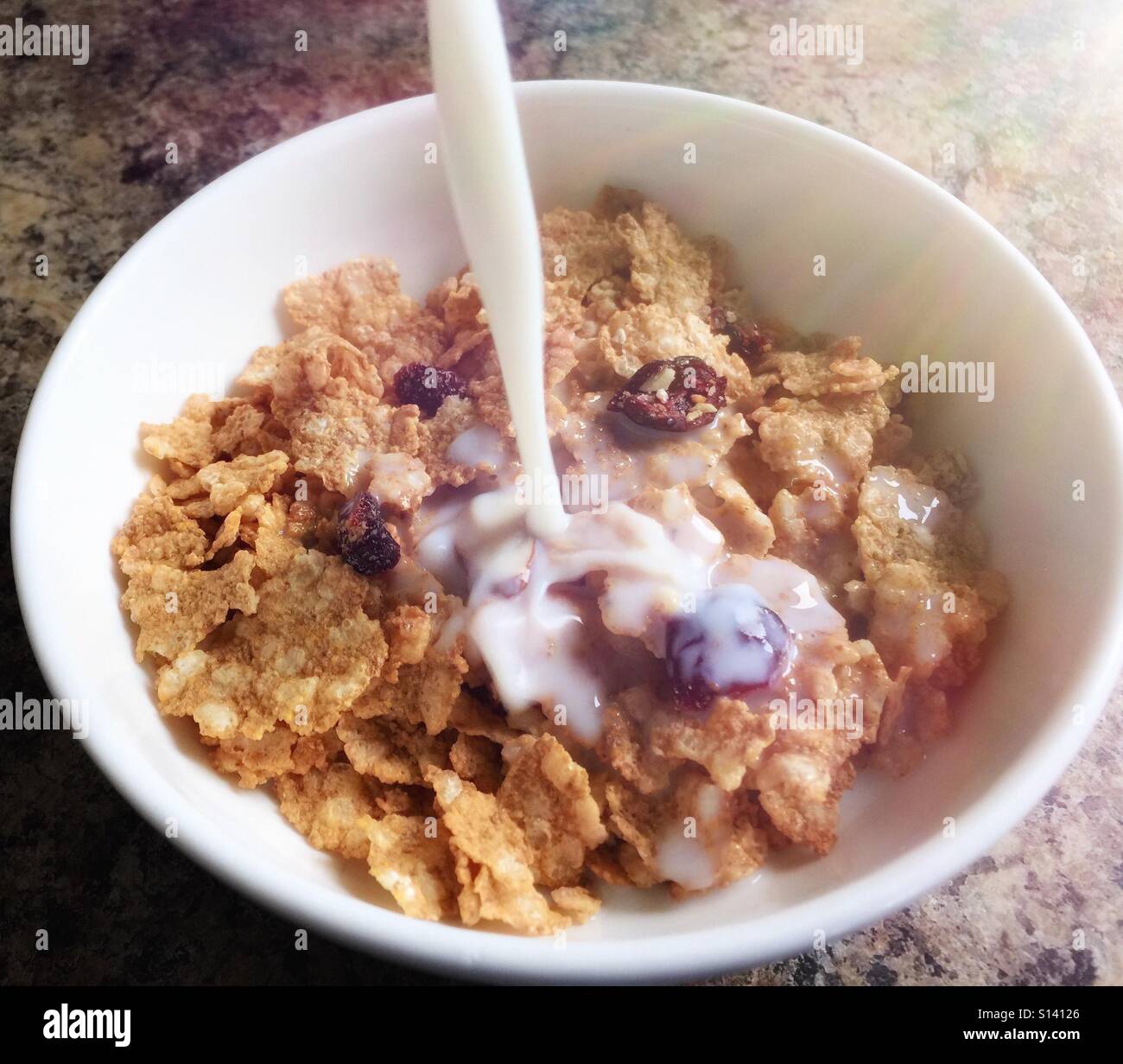 Morgensonne bescheint eine Schüssel Müsli, wie oben Milch übergossen wird. - Smartphone-aufgenommenes Stockfoto