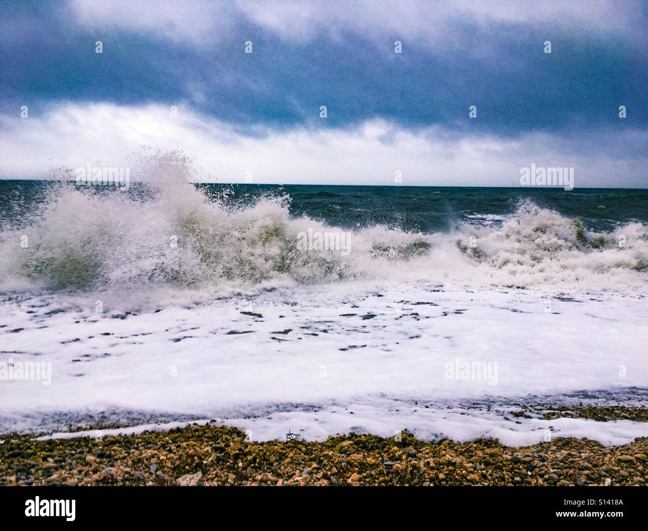 Wellen brechen sich am Strand mit Gewitterwolken oben. Stockfoto