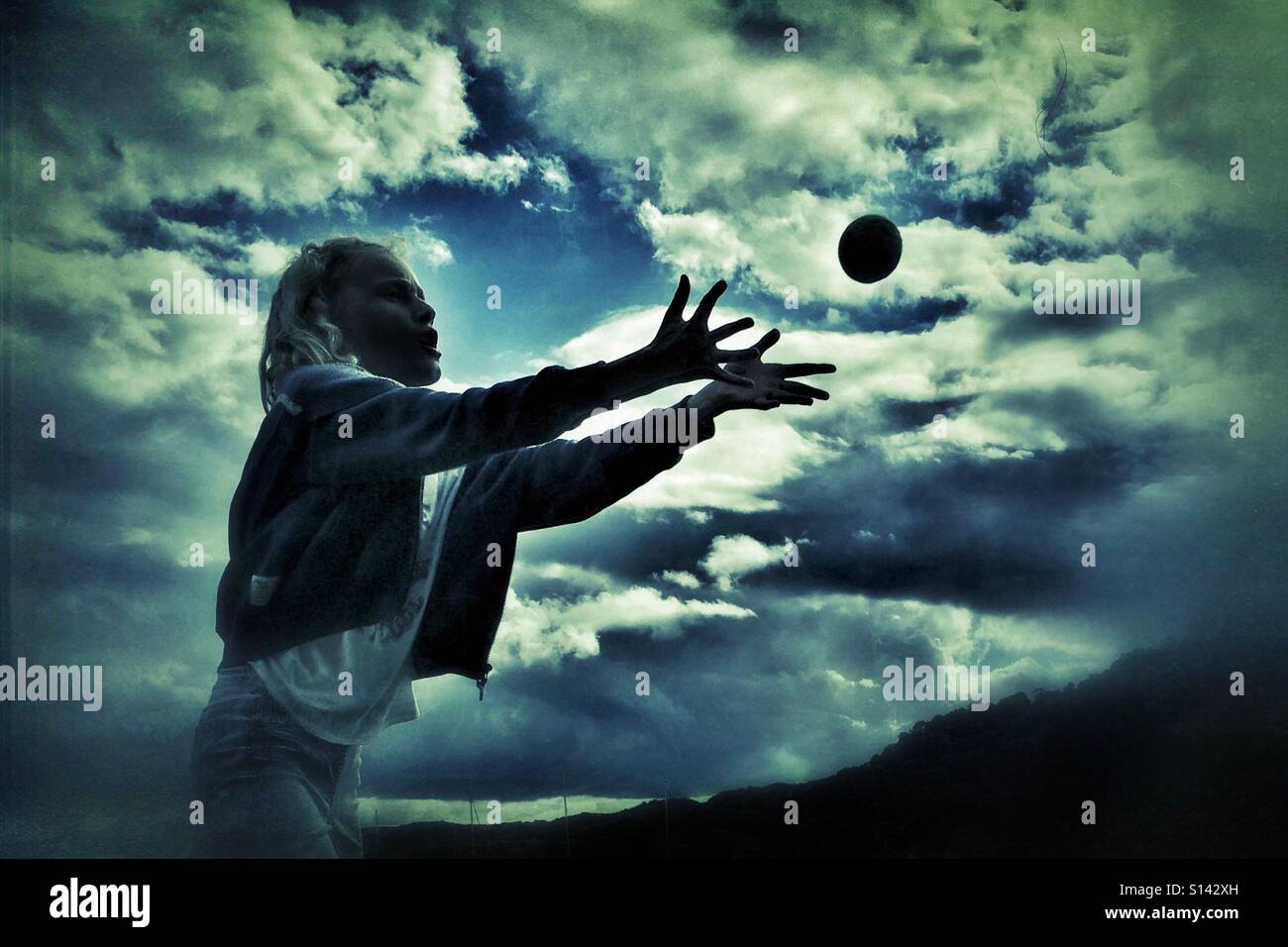 Junges Mädchen Ball gegen einen dramatischen Wolkenhimmel fängt Stockfoto