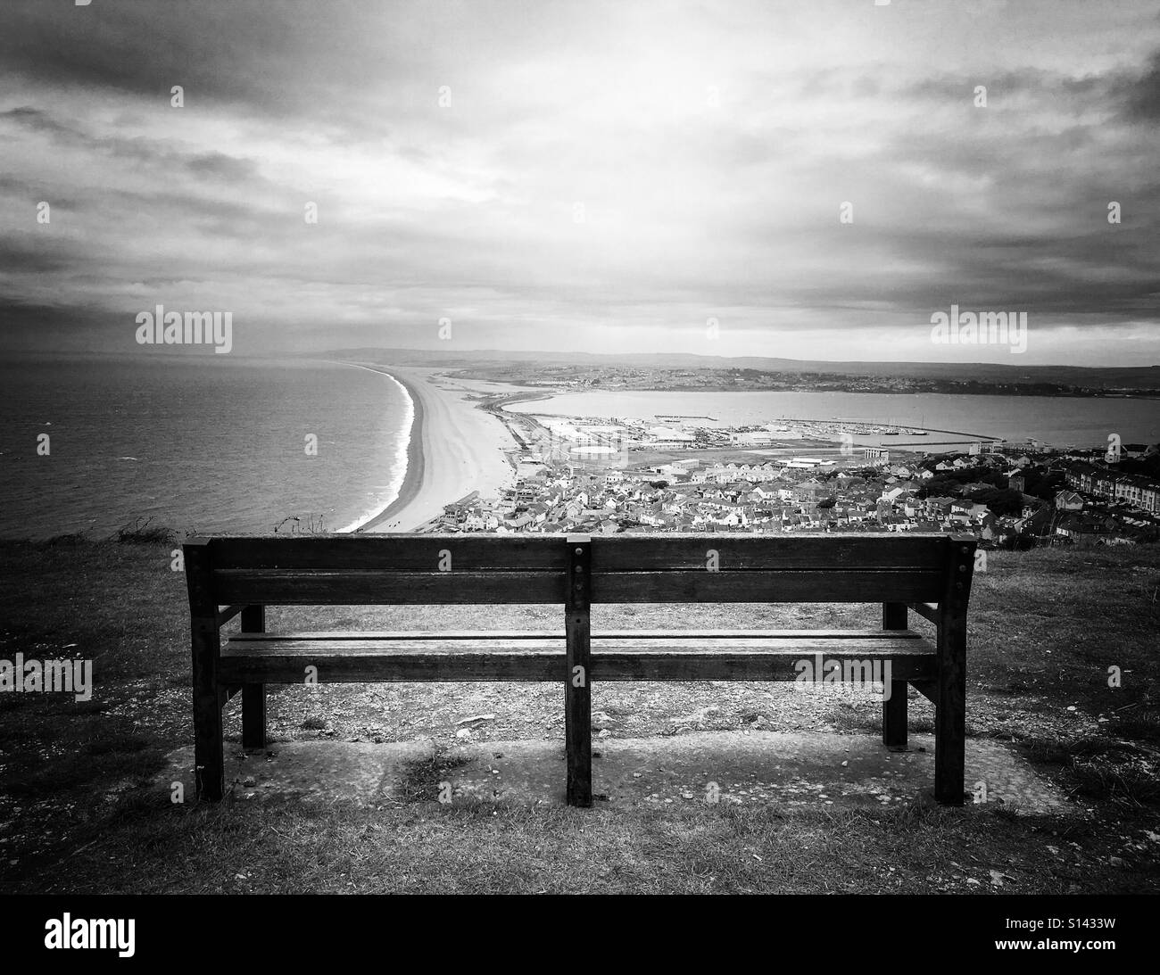 Lichtstrahl trifft einsame Park bench mit Blick auf Hafen von Weymouth. Stockfoto