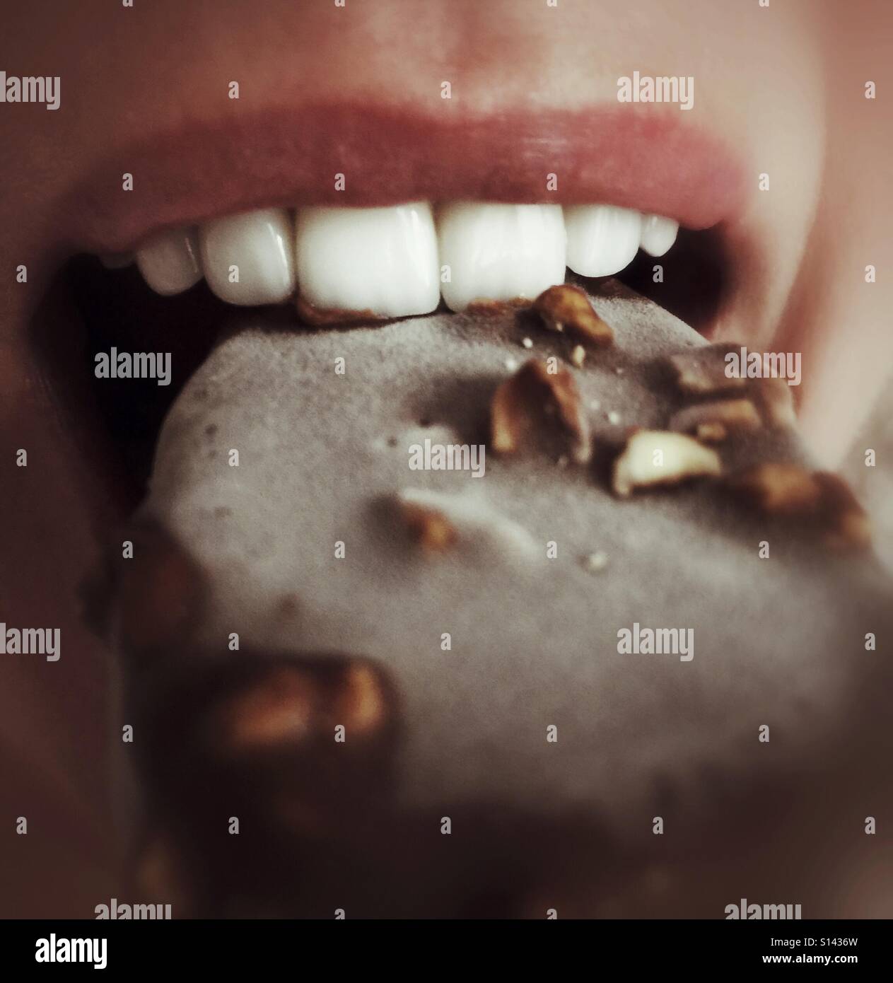 Zähne beißen in eine Nuss und Schokolade bedeckten Eis-Bar. Stockfoto