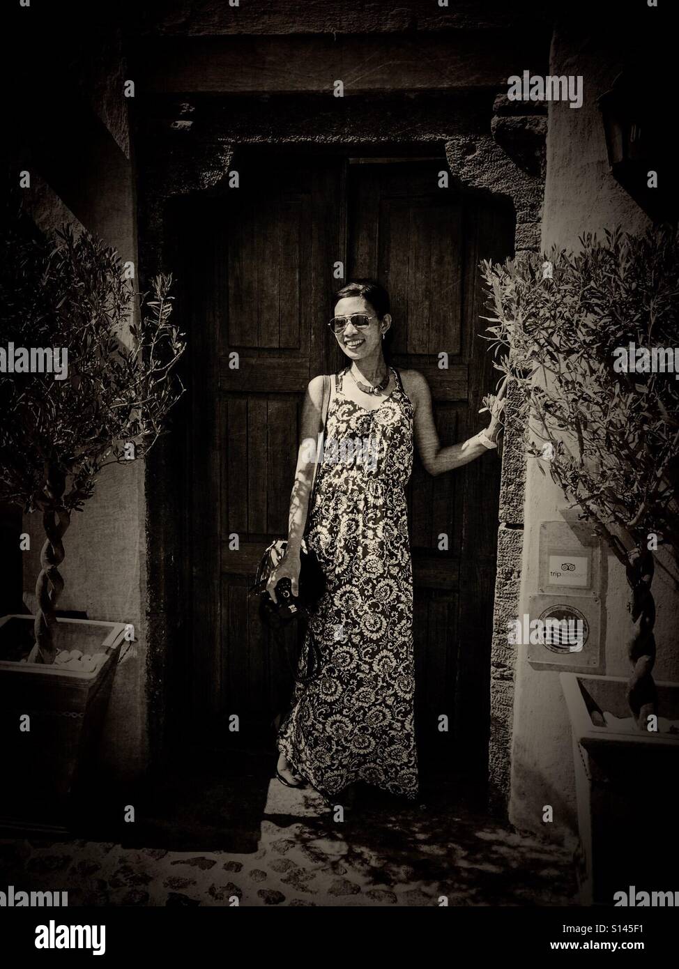 Eine Dame posiert in einem Hauseingang in Oia auf der griechischen Insel Santorin. - Smartphone-aufgenommenes Stockfoto