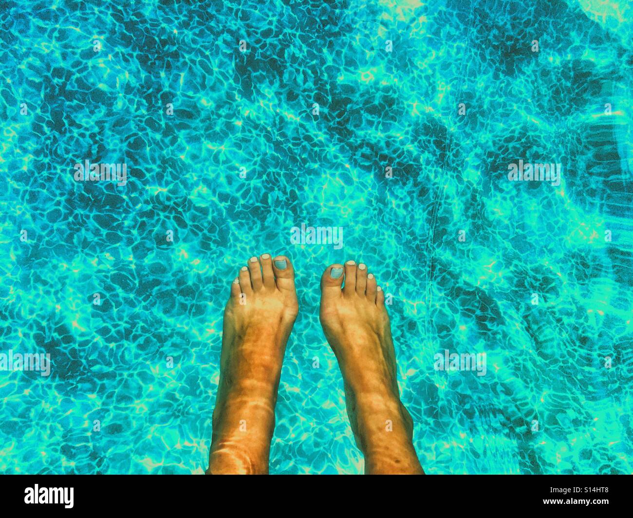 Füße im Pool, Sonne auf dem Wasser reflektiert. Stockfoto