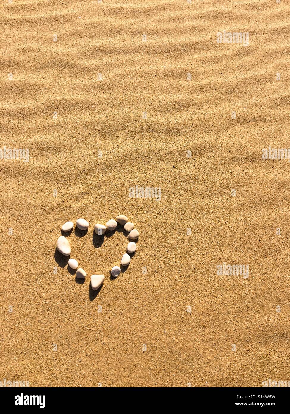 Herzen von kleinen, weißen Kieselsteinen an einem goldenen Sandstrand gebildet - Smartphone-aufgenommenes Stockfoto