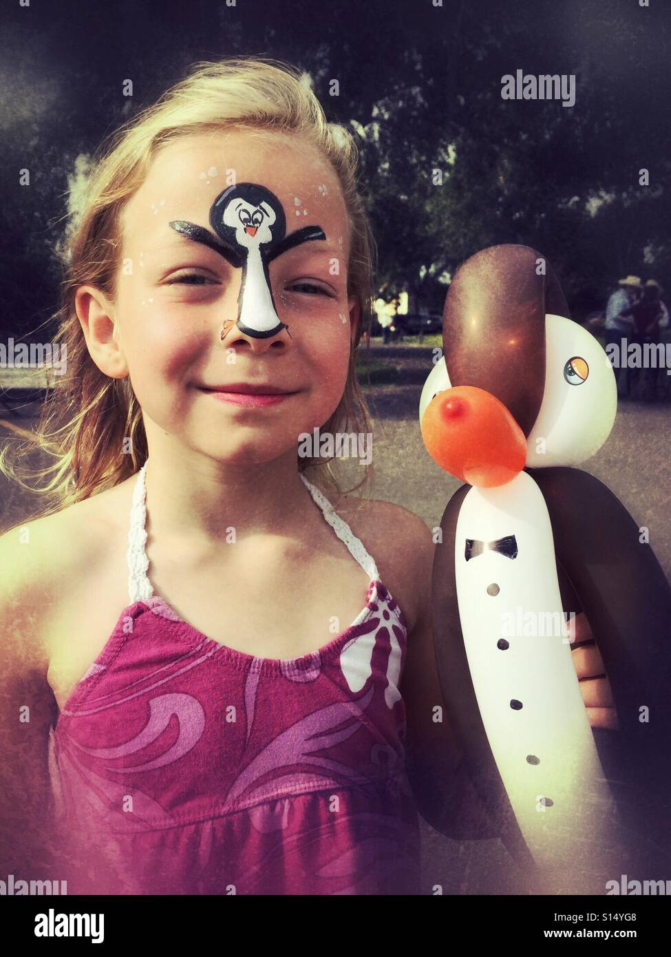 Eine Mädchen mit einem Pinguin auf ihr Gesicht, hält einen Pinguin-förmigen Ballon gemalt. - Smartphone-aufgenommenes Stockfoto
