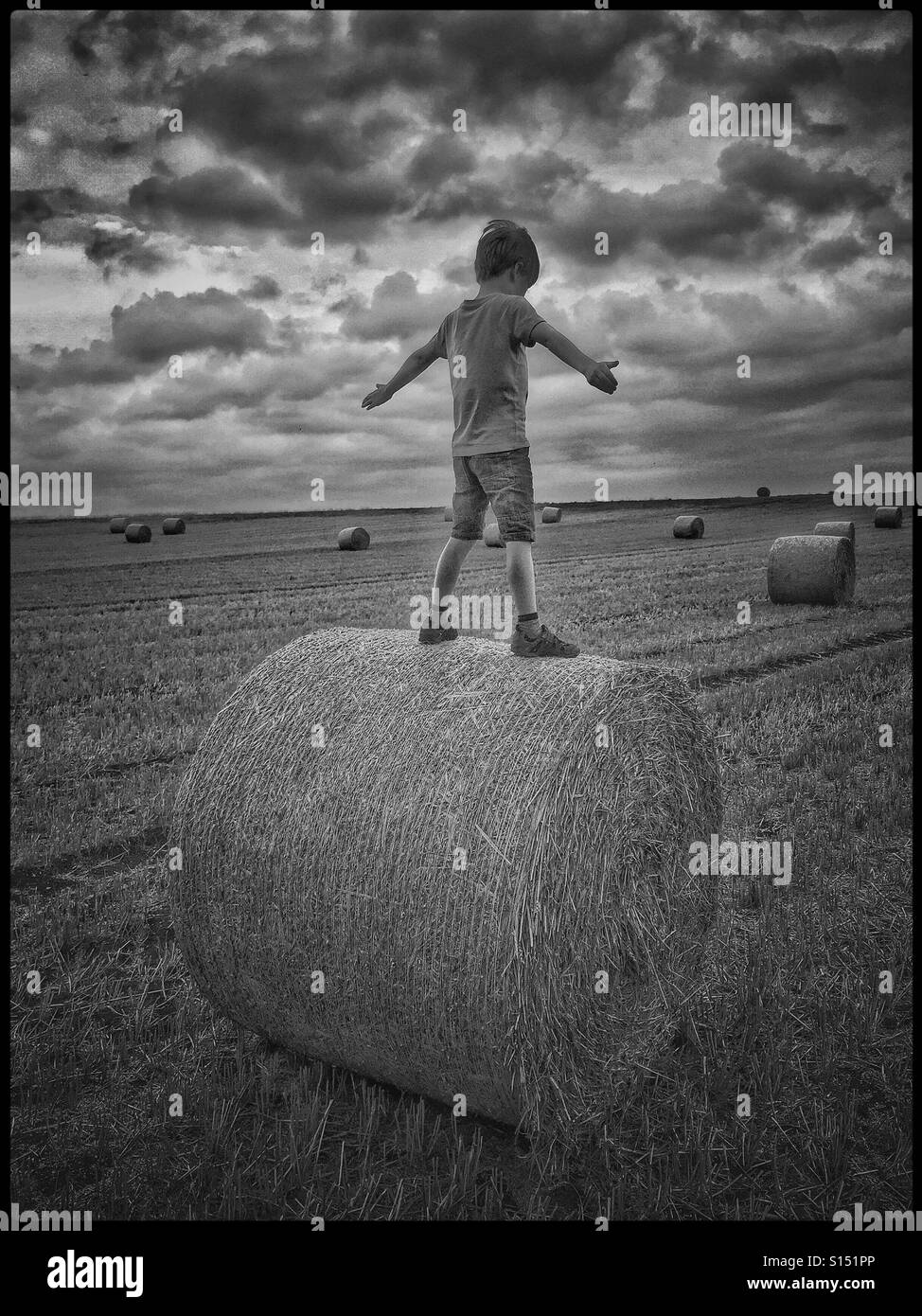 Ein 7 Jahre alter Junge balanciert auf einer kürzlich produzierten Heuballen. Die Lage ist ein offenes Feld im Süden von England. Ein Bild zur Veranschaulichung der unbeschwerten Freuden der Kindheit. Kredit - © COLIN HOSKINS - Smartphone-aufgenommenes Stockfoto