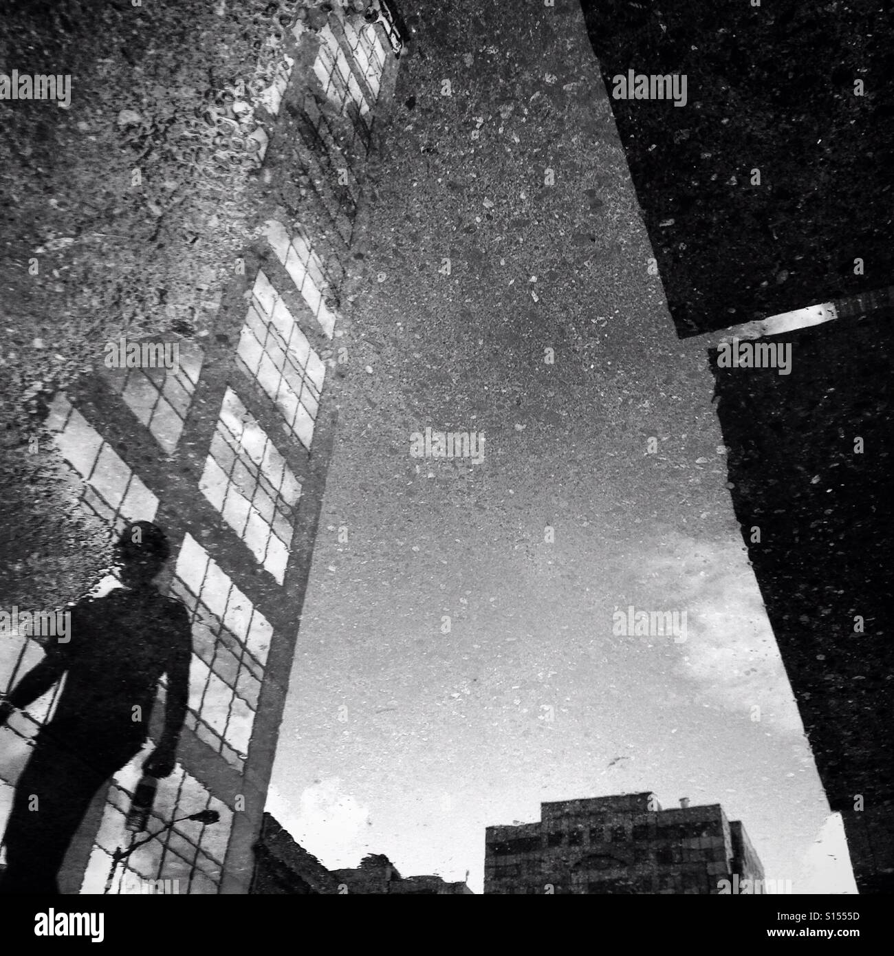 Eine Person und ein Gebäude spiegeln sich in einer Pfütze in einem städtischen Umfeld Stockfoto