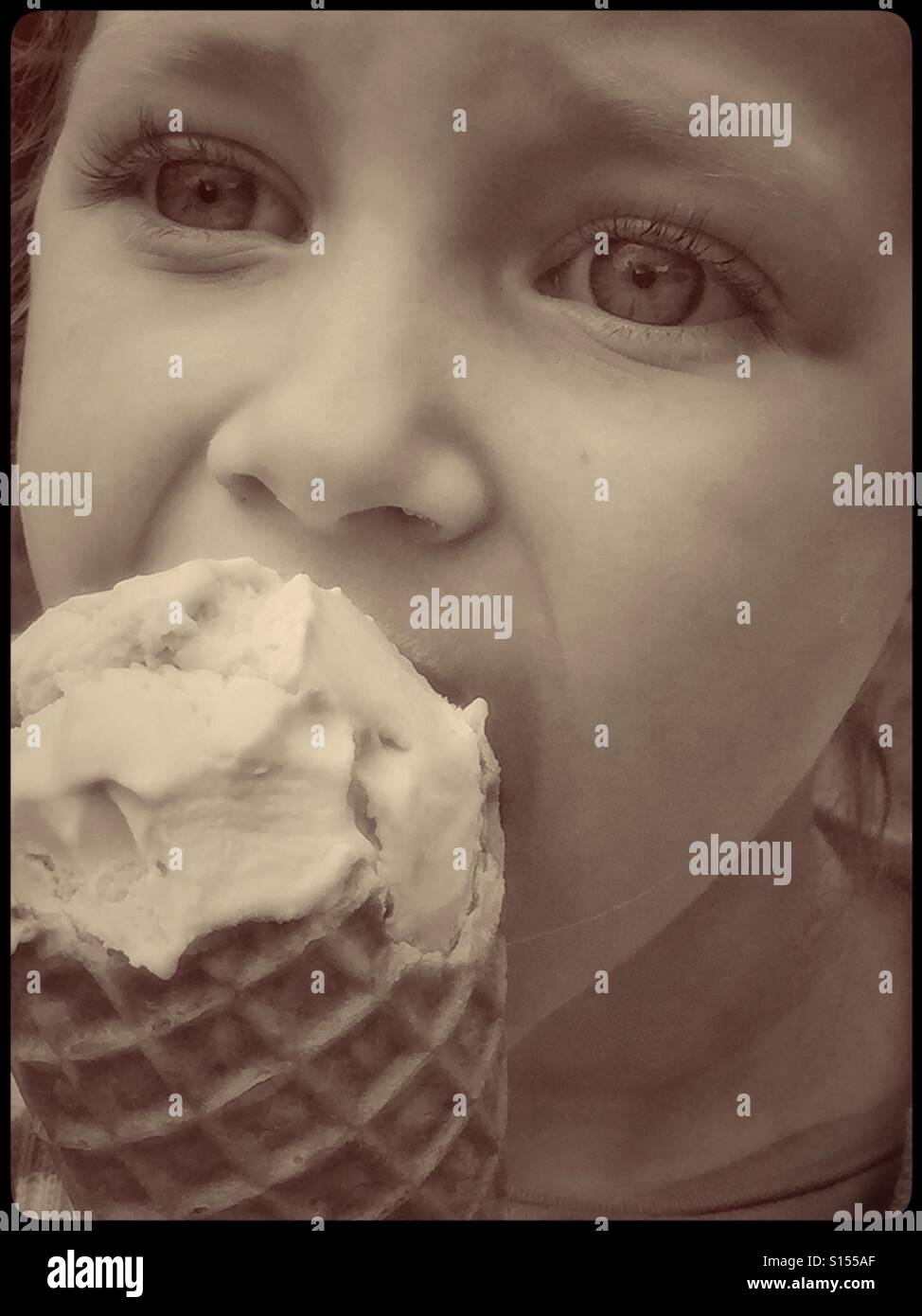 Eine Nahaufnahme, Sepia getönten Bild eines 4 Jahre alten Mädchens einen großen Kegel gefüllt mit Vanilleeis Essen. Die Freuden der Kindheit und im Sommer! Foto Credit © COLIN HOSKINS. Stockfoto