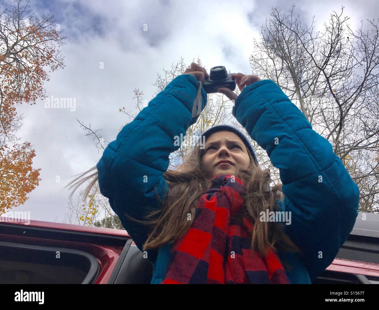 Eine Tween-Mädchen mit langen braunen Haaren und einem karierten Schal lehnt sich aus einem Autofenster auf ein Foto. Stockfoto