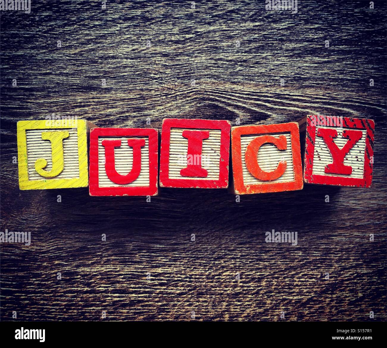 JUICY Wort geschrieben mit Holzblock-Buchstaben-Spielzeug mit Alphabet-Buchstaben-Design - Smartphone-aufgenommenes Stockfoto