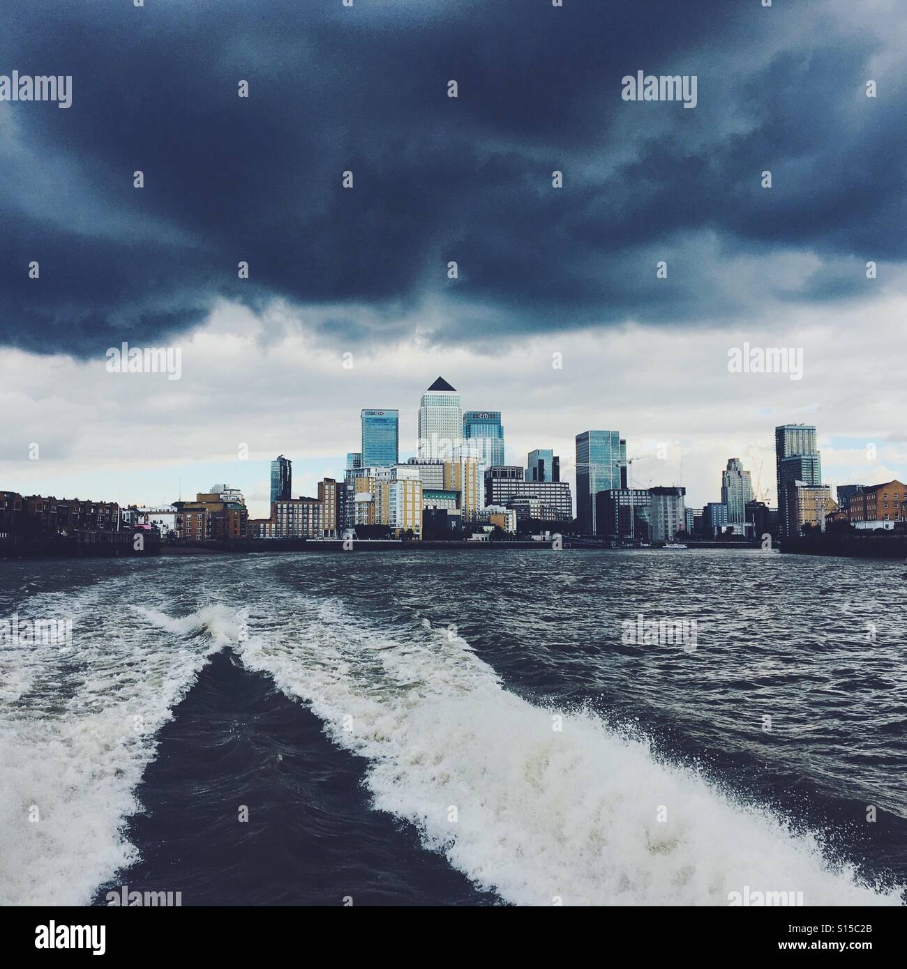 Skyline von London Docklands von einem Boot auf der Themse mit stürmischen Wolken gesehen. Stockfoto