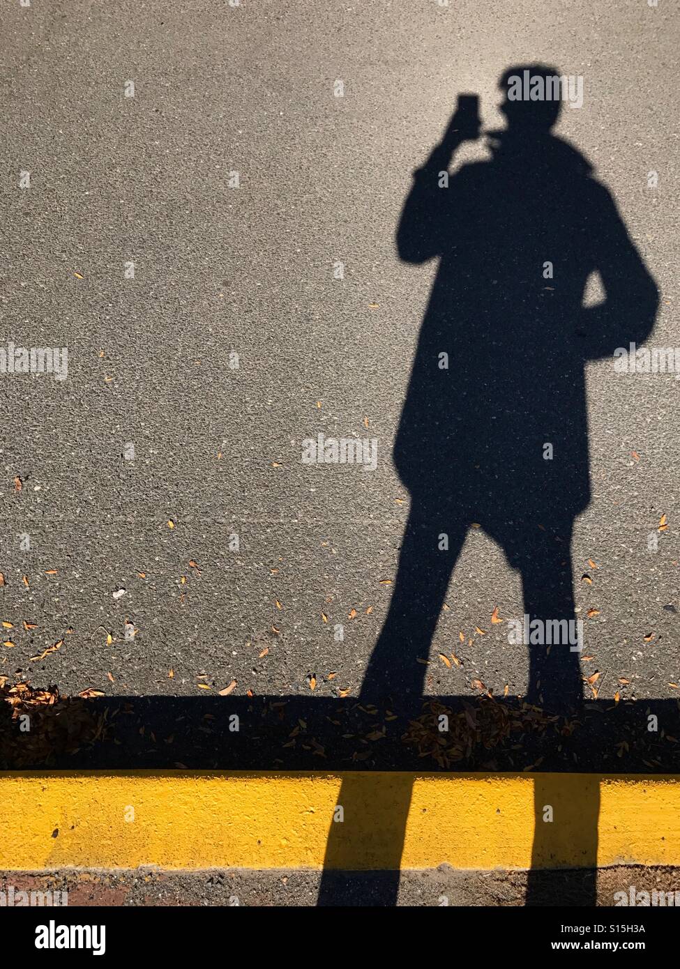 Schatten eines Menschen mit einem Smartphone auf einem Bürgersteig/Pflaster. - Smartphone-aufgenommenes Stockfoto