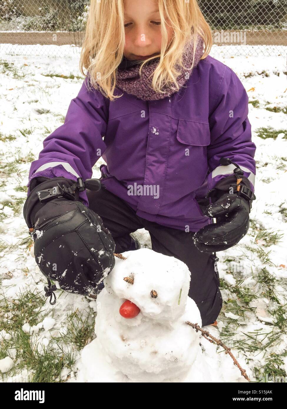 Eine Mädchen setzt letzten Schliff auf ihren Schneemann. Stockfoto