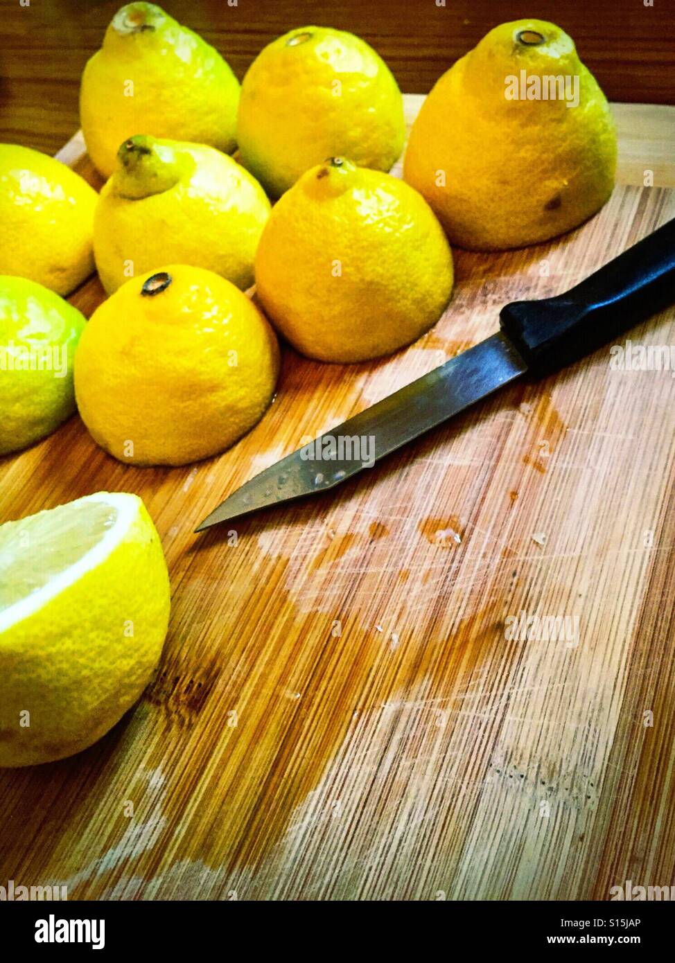 Halbierte Zitronen und ein Messer auf ein Schneidbrett aus Holz. - Smartphone-aufgenommenes Stockfoto