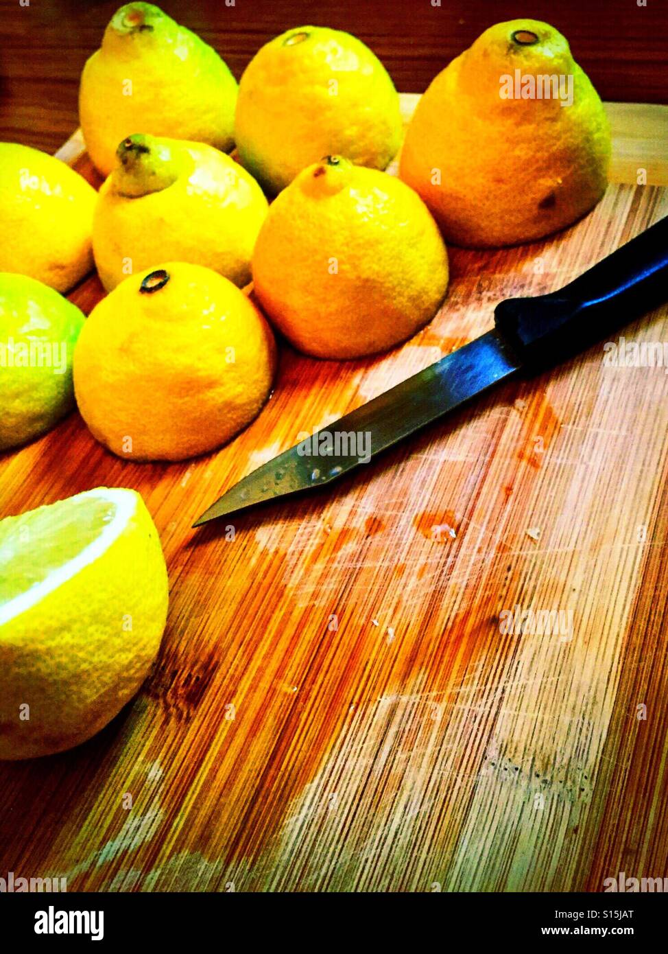 Halbierte Zitronen und ein Messer auf ein Schneidbrett aus Holz. - Smartphone-aufgenommenes Stockfoto