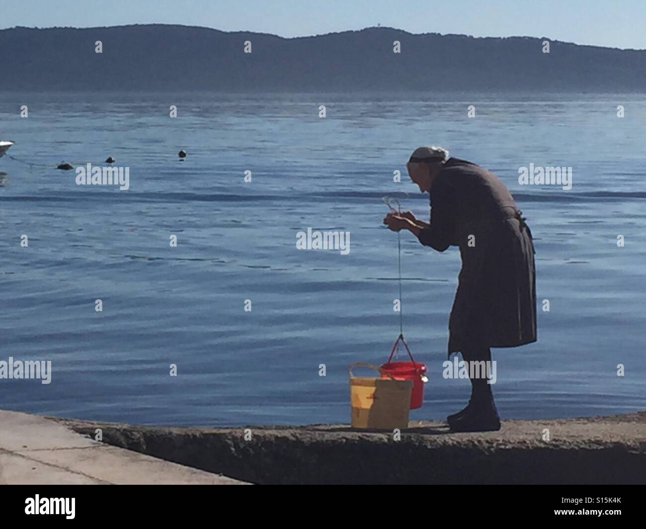 Alte Dame Abholung Meerwasser in Kastela, Kroatien - Smartphone-aufgenommenes Stockfoto