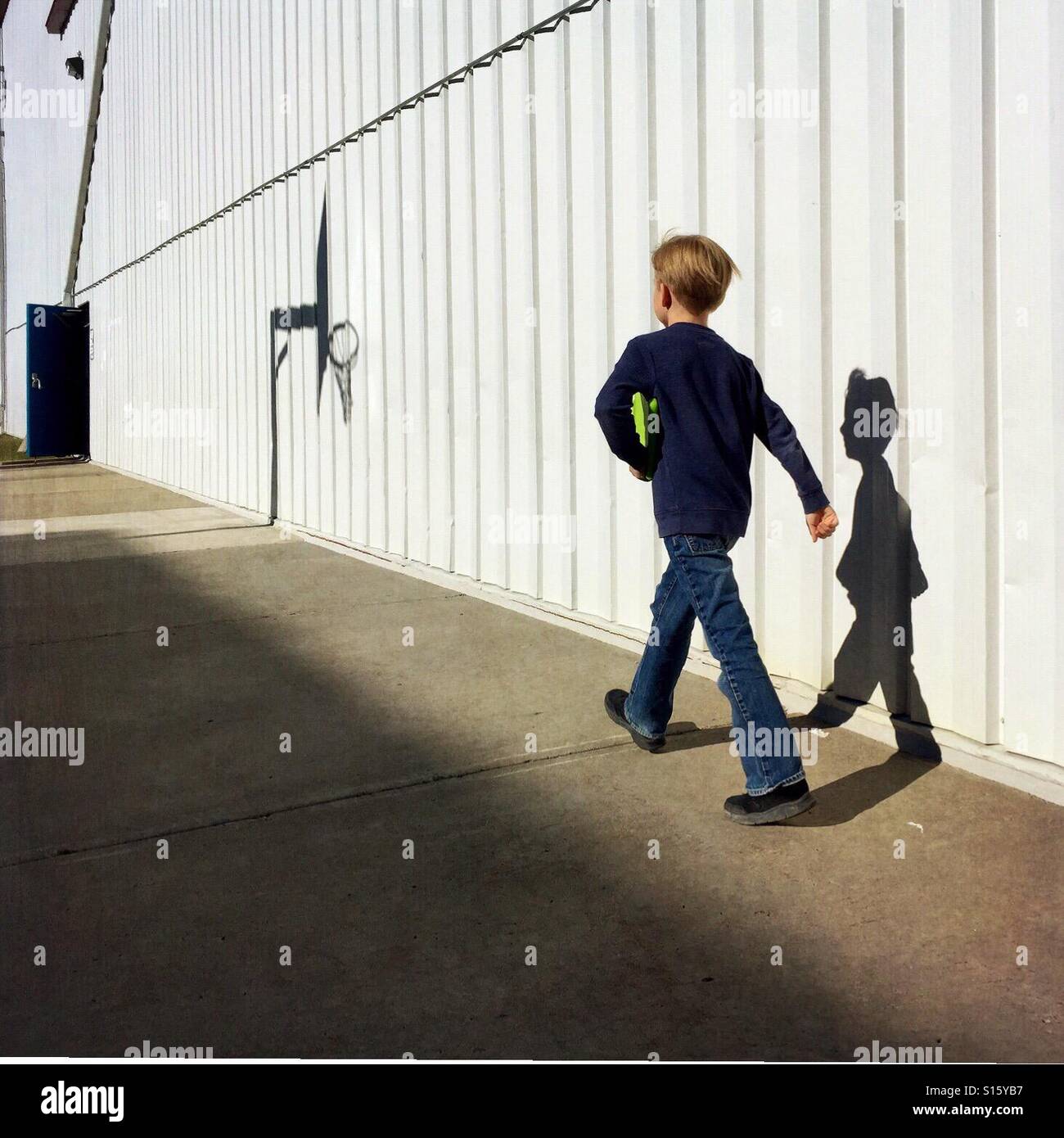 Ein Junge mit seinem Tablet unter dem Arm geht munter neben einem Geschäftshaus in Richtung einer offenen Tür. Stockfoto