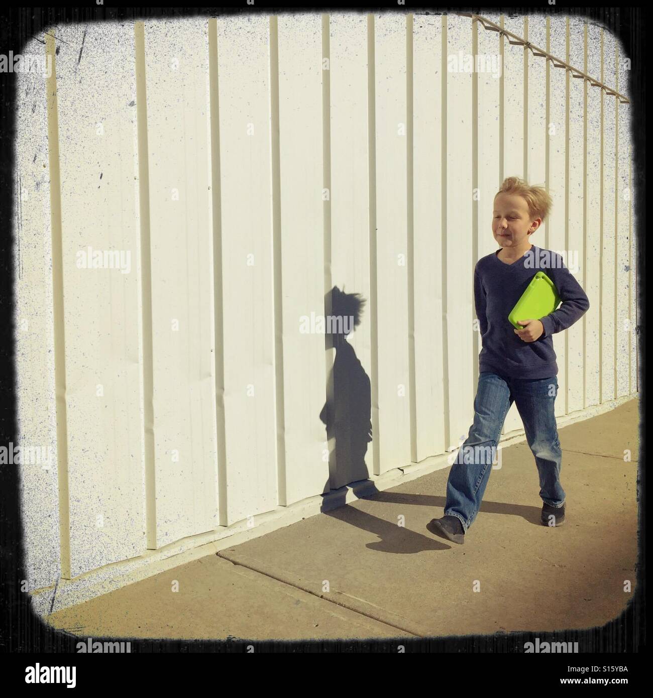 Ein Junge mit seinem Tablet unter dem Arm geht zügig entlang eines Gebäudes. Stockfoto