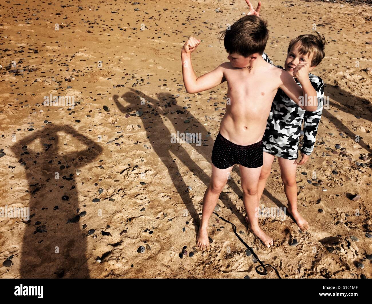 Ein 11 jähriger Junge beugt seine Muskeln vor seinem jüngeren Bruder auf Süßwasser Weststrand in Wales. Stockfoto