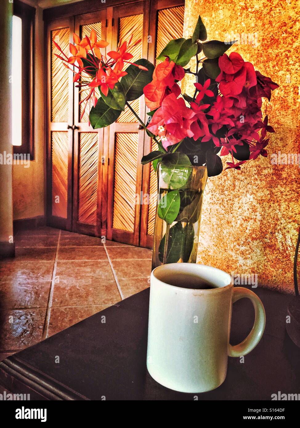 Eine Tasse Kaffee und eine Vase mit Blumen sind auf einem Nachttisch in ein schönes Schlafzimmer in Nayarit, Mexiko. Stockfoto