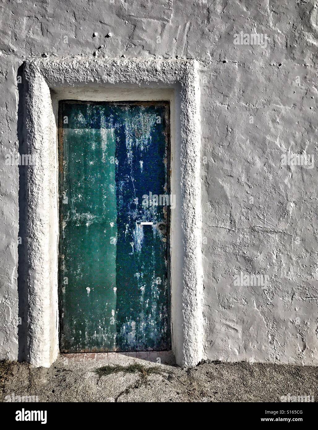 Stark verwitterte Tür blau lackiert und grün mit eine grobe Darsteller brillant weiße Betonwand von Immobilien an der Küste im Süden Spaniens in der Nähe von Caleta de Velez mit Blick aufs Meer. Stockfoto