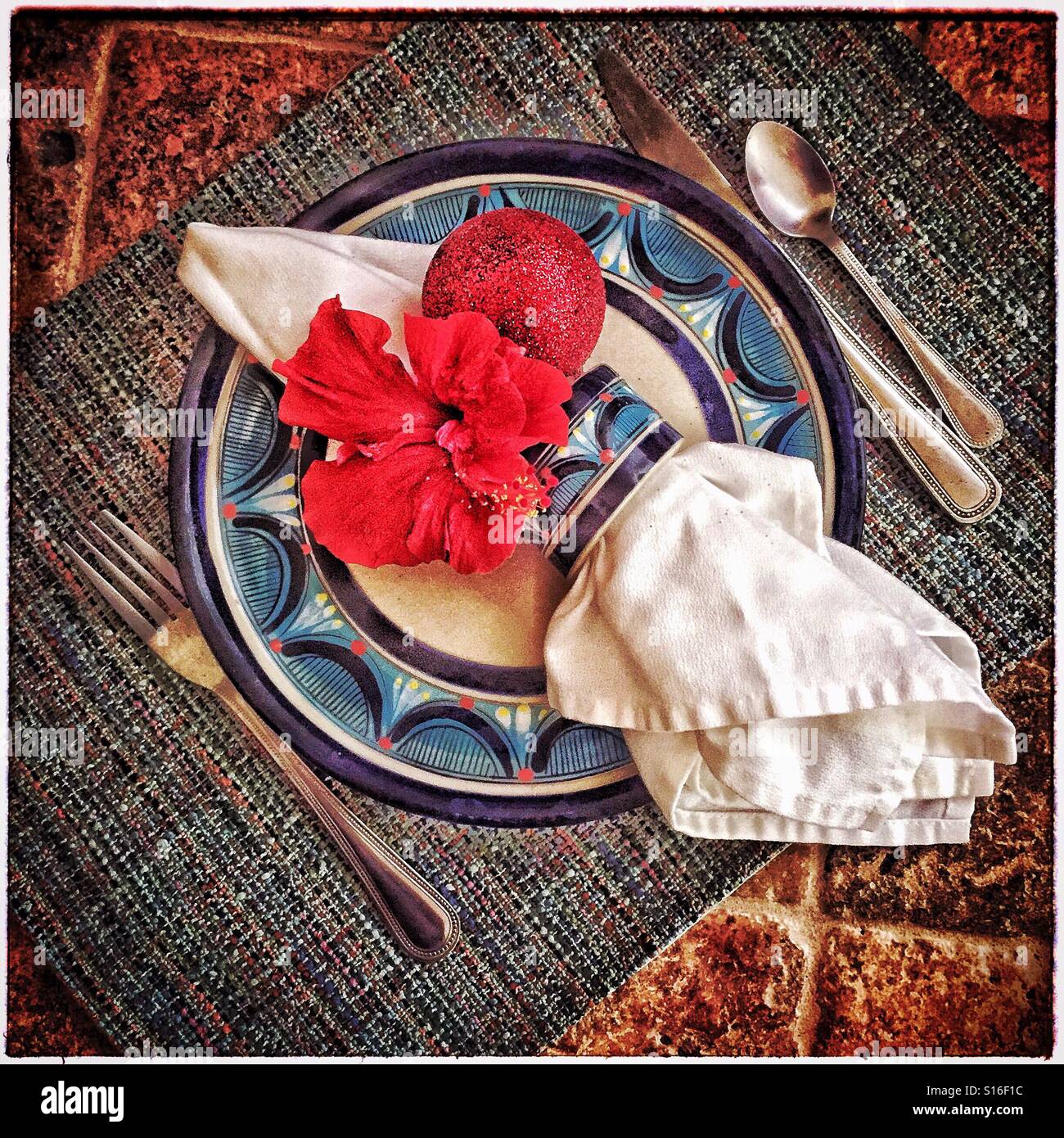 Ein Urlaub-Gedeck mit einer frischen roten Hibiskus Blume und ein glitzerndes rot Ornament in der Serviettenring auf einer lackierten Platte. Stockfoto
