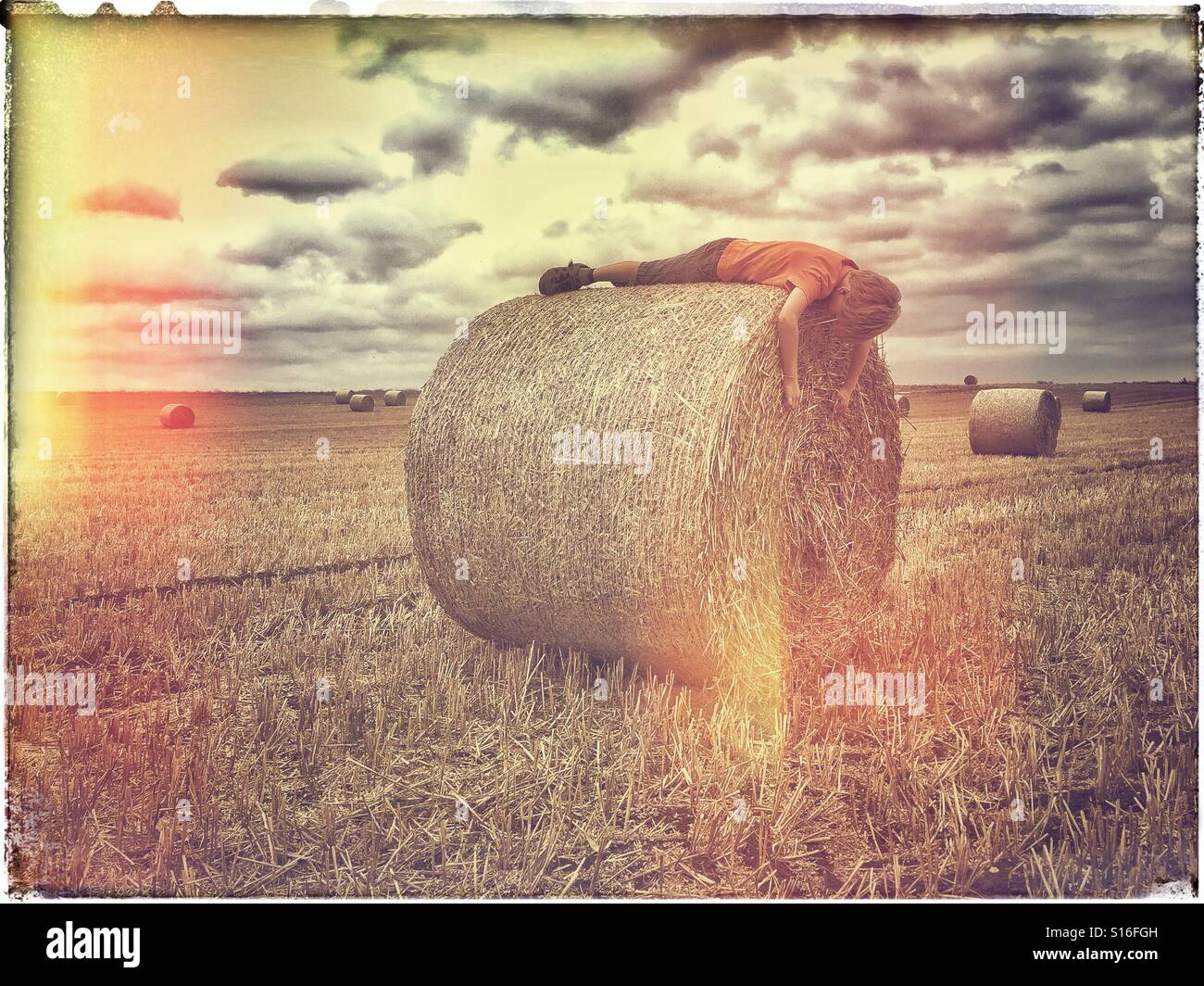 Eine analoge (Film mit leicht beschlagen) Effekt Bild eines 6 Jahre alten Jungen auf einer frisch hergestellten Heuballen liegen. Es ist Erntezeit & der junge scheint allein in einem Feld zu sein. Schläft er? © COLIN HOSKINS. - Smartphone-aufgenommenes Stockfoto