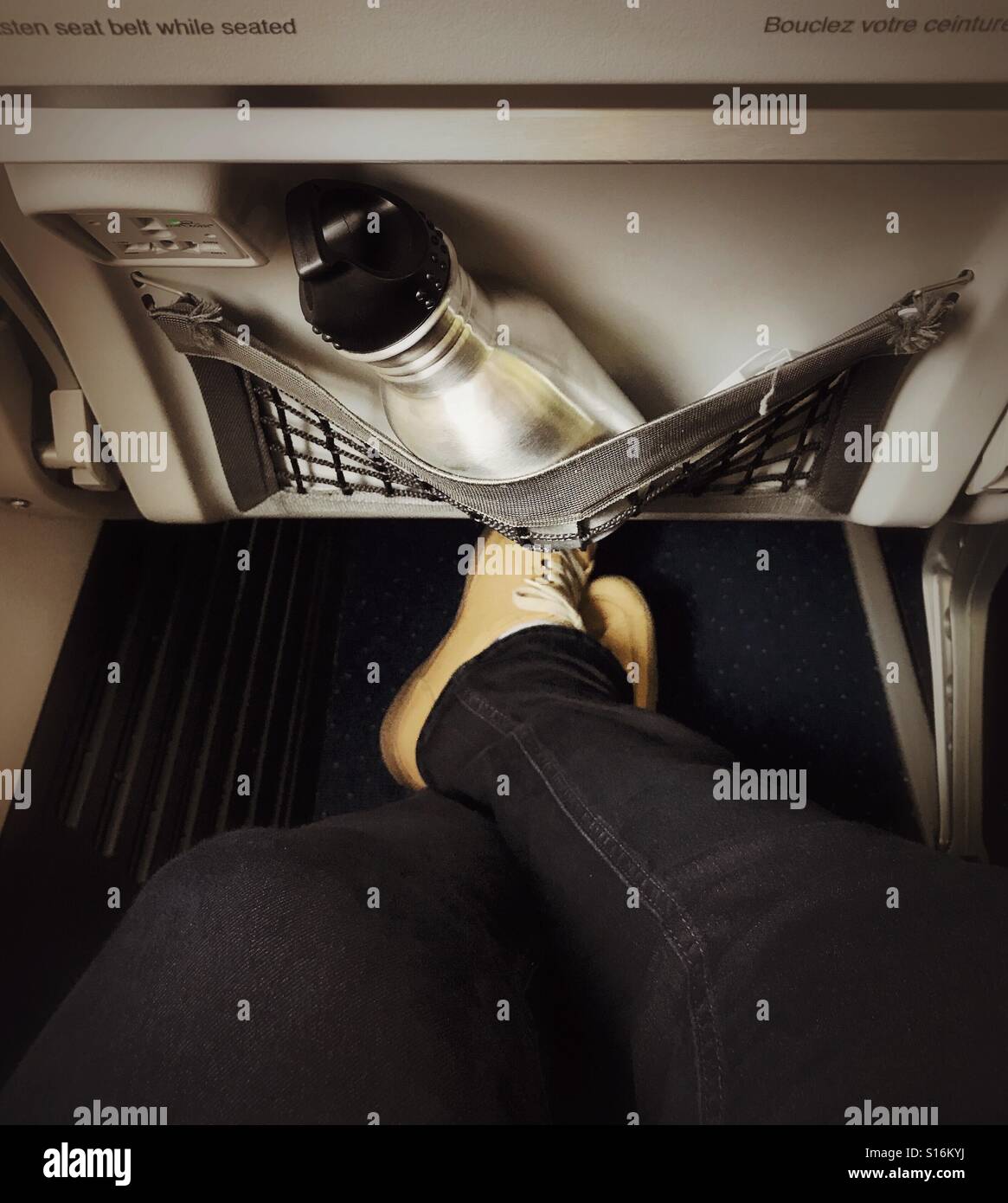 An den Knöcheln und eine Flasche Wasser in die Beinfreiheit von einem kommerziellen Passagierflugzeugen gekreuzten Beinen. Stockfoto