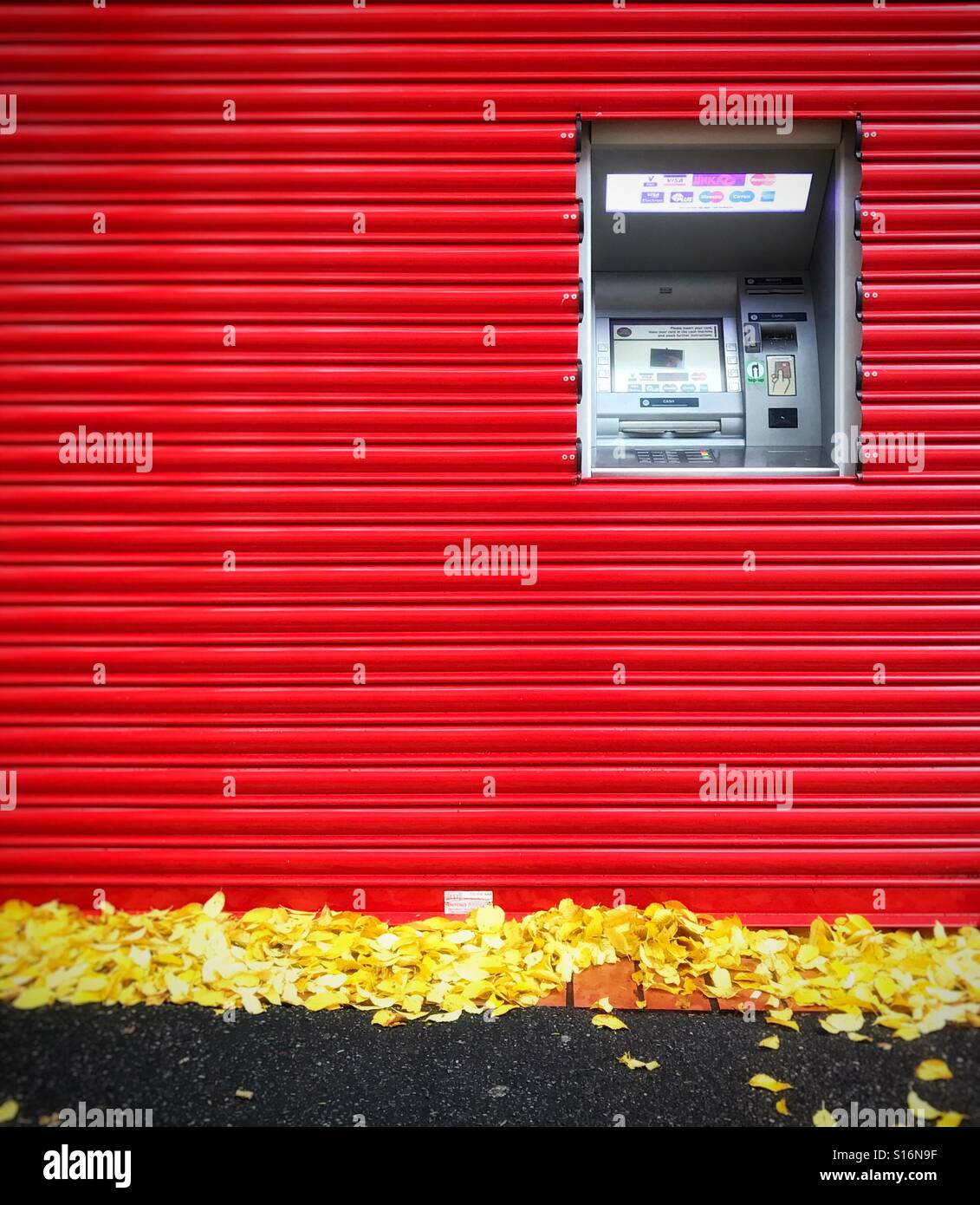Geldautomaten, die umgeben von leuchtend roten Fensterläden - Smartphone-aufgenommenes Stockfoto