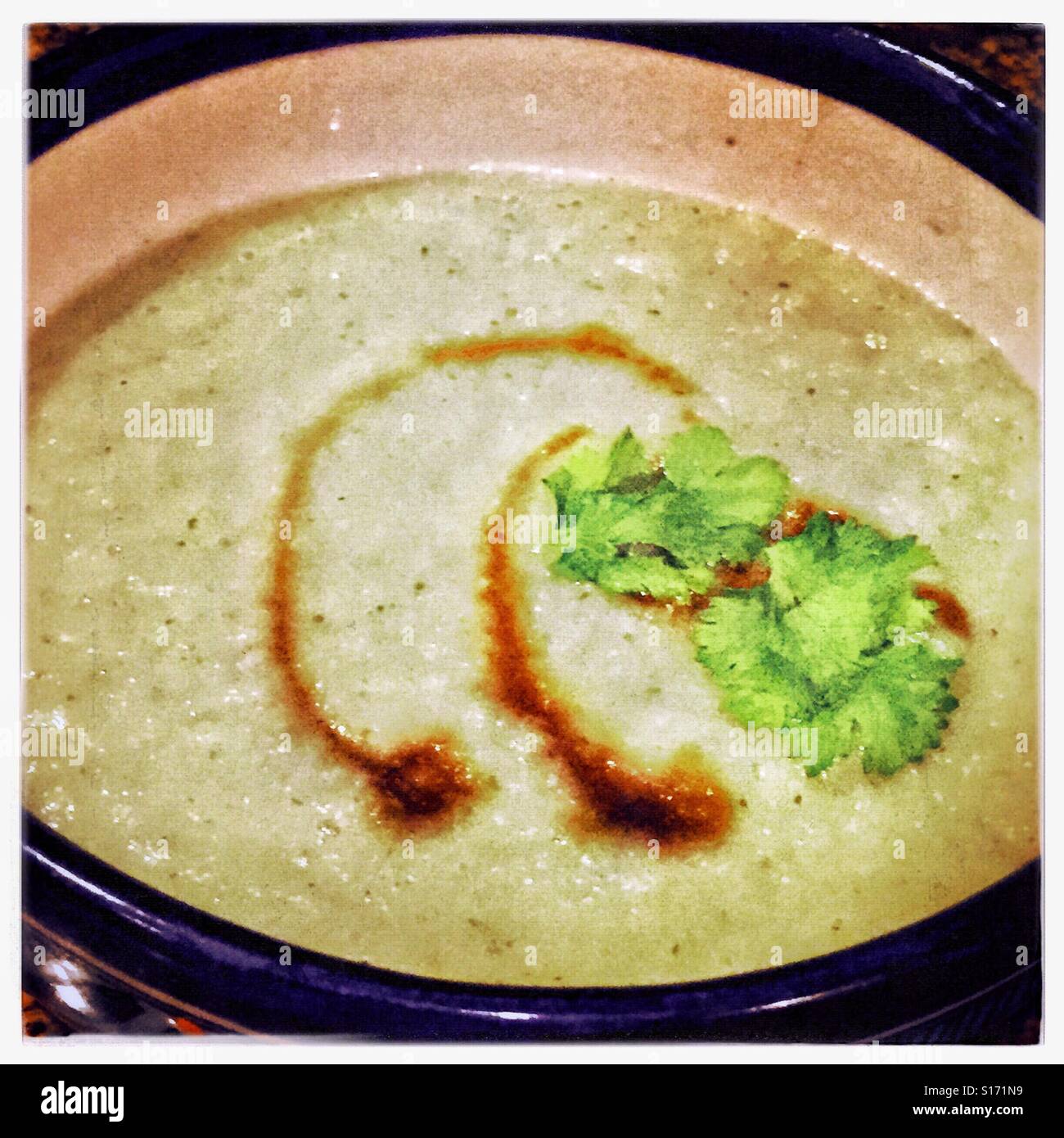 Chayote Suppe in eine Schüssel geben, garniert mit einem Schuss rauchige süße Chipotle Sauce und Koriander Blätter. Stockfoto