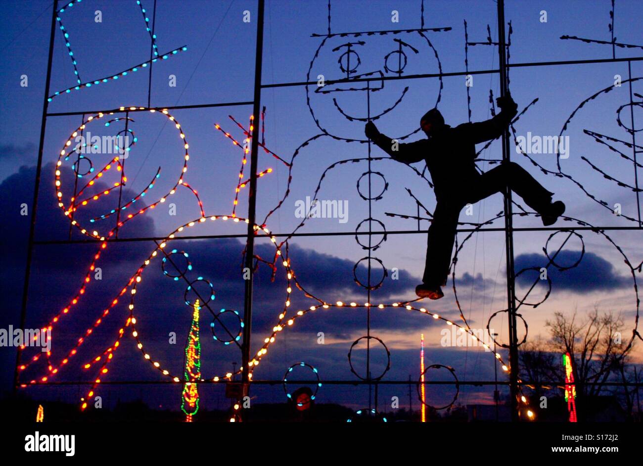 Ein Mann klettert auf einen Rahmen zu Weihnachten Dekorationen beleuchtet für den Urlaub - Smartphone-aufgenommenes Stockfoto