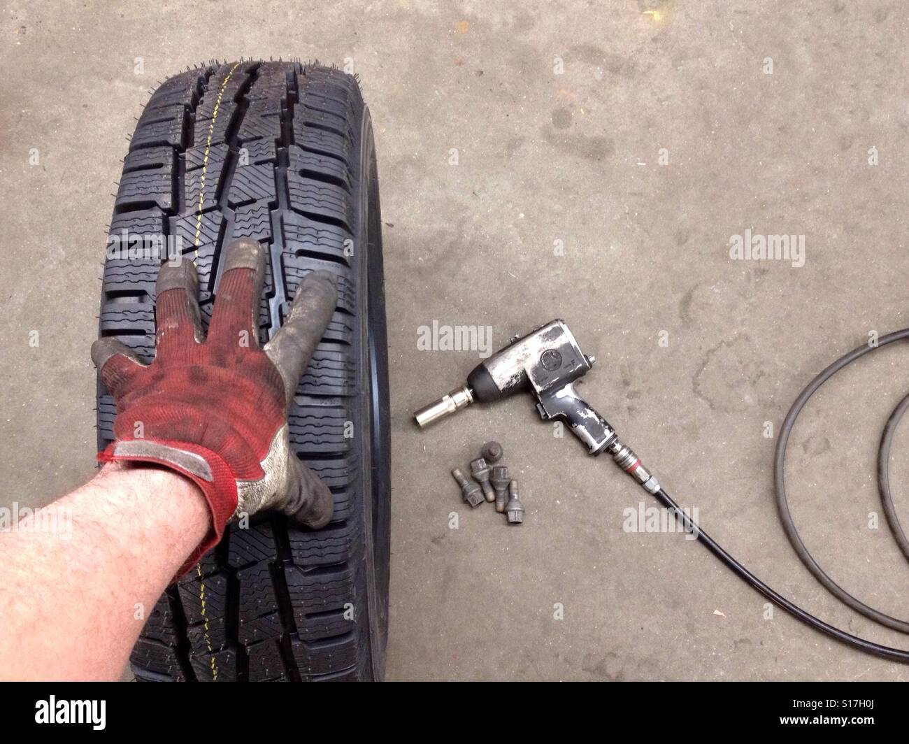 Mechaniker im Besitz einer Hand auf einem Autoreifen, auf dem Boden ist ein Rad-Pistole und Rad Muttern - Smartphone-aufgenommenes Stockfoto