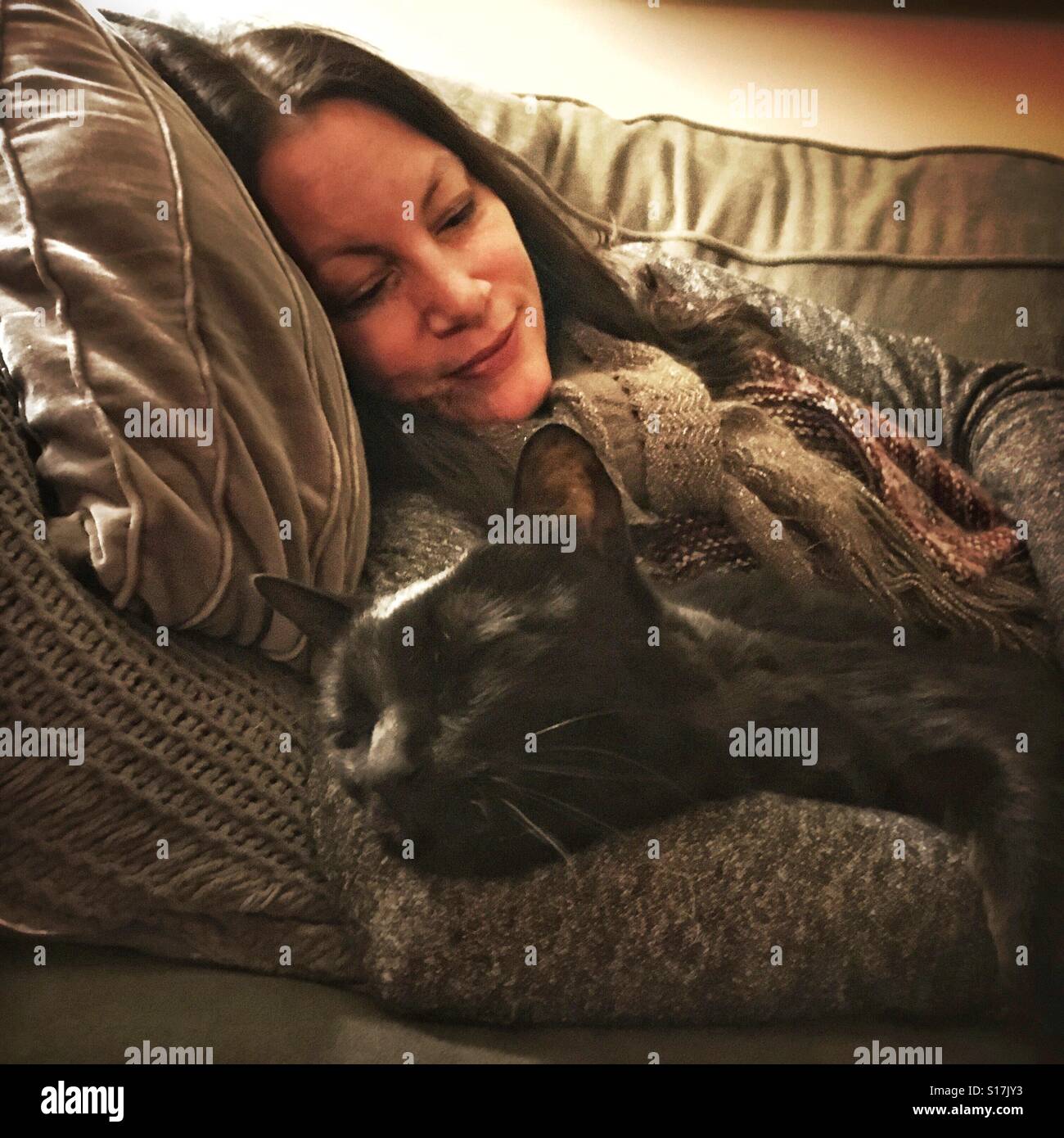 Frau auf Sofa mit Haustier Katze kuscheln - Smartphone-aufgenommenes Stockfoto