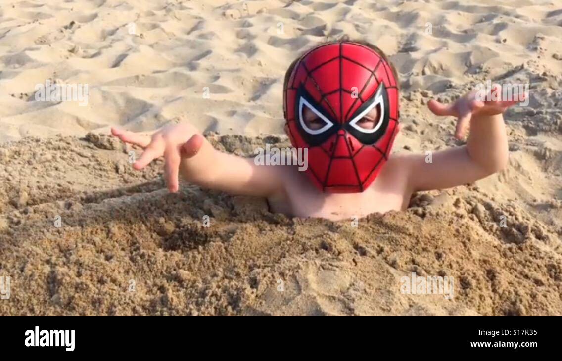 Boy am Strand mit Spider-Man Maske Stockfoto