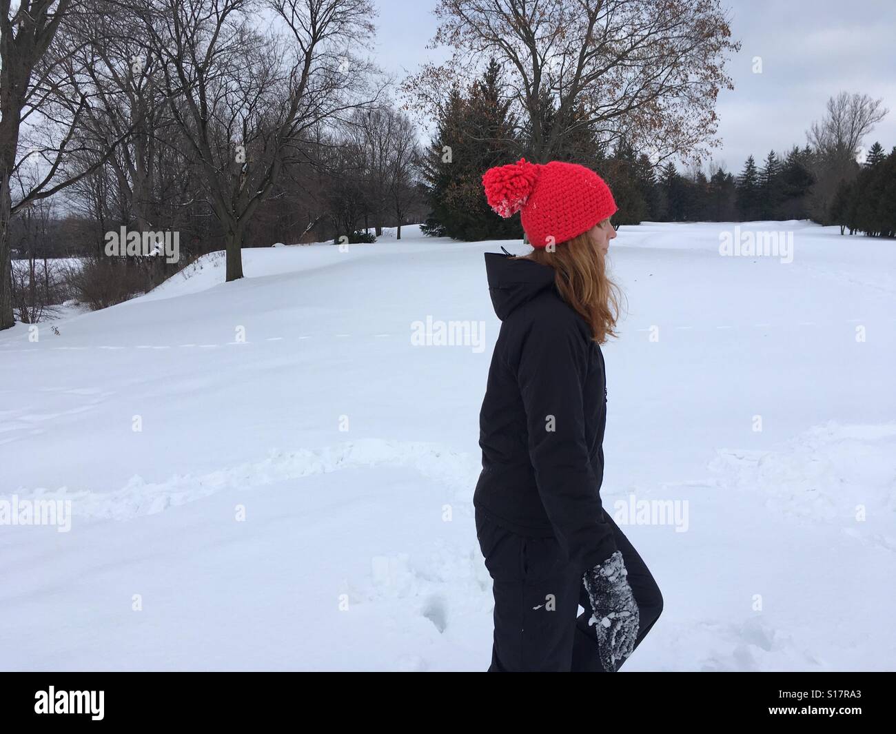 Mädchen draußen im Schnee mit einem roten Hut auf - Smartphone-aufgenommenes Stockfoto